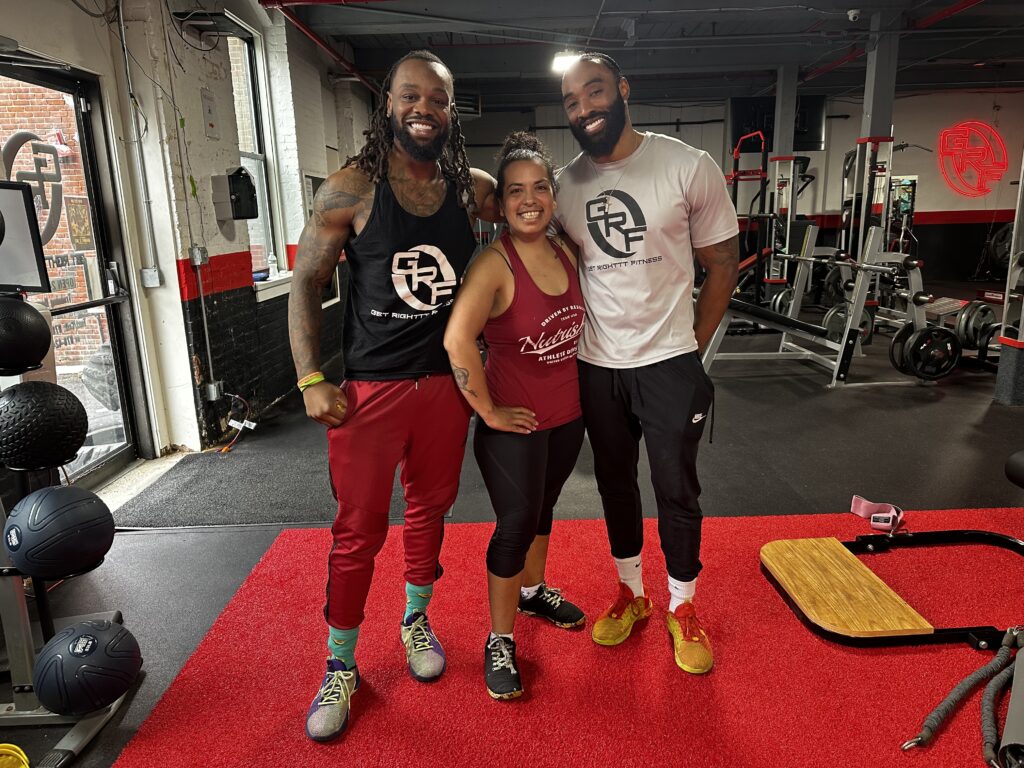 Julie Whitley stands with two fellow fitness coaches in a gym, smiling after a workout session, representing teamwork, strength, and motivation.